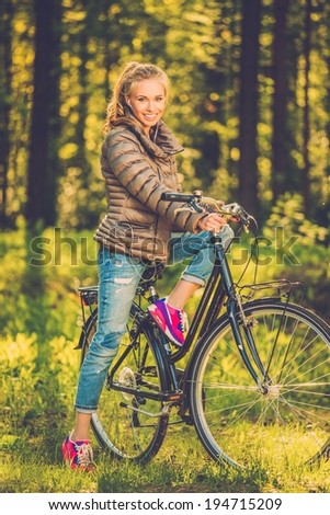 Cheerful teenage girl listens music on a bicycle outdoors