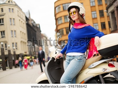 Young cheerful girl near scooter in in european city