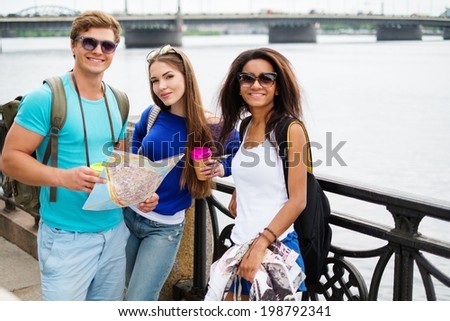 Multi-ethnic friends tourists with map and coffee cups near river in a city