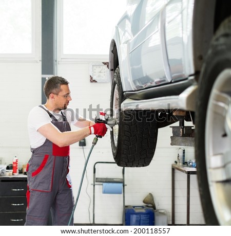 Serviceman unscrewing wheel in car workshop