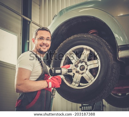 Cheerful serviceman unscrewing wheel in car workshop