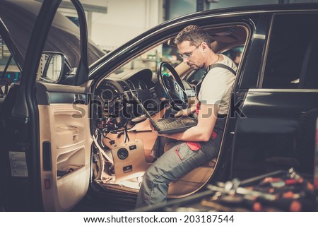 Serviceman making car diagnostics with laptop in a workshop