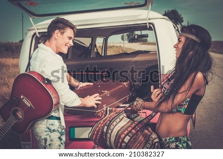Multi-ethnic hippie couple with guitar packing luggage for a road trip