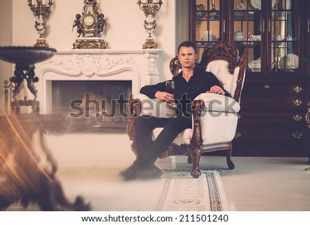 Handsome well-dressed man sitting with red wine in luxury  house interior