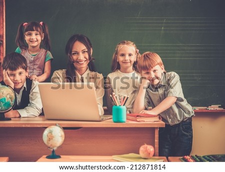 Group of happy classmates with their teacher in class near blackboard