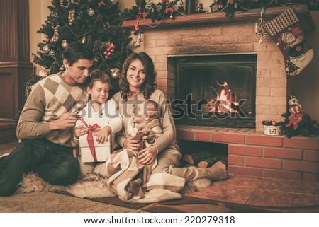 Family near fireplace in Christmas decorated house interior with gift box