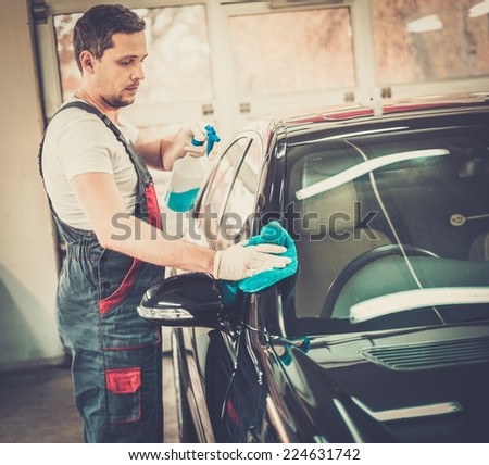 Worker on a car wash cleaning car with a spray