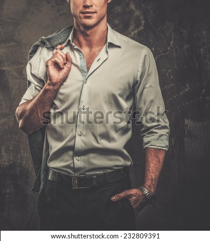 Handsome man in shirt against grunge wall holding jacket over shoulder