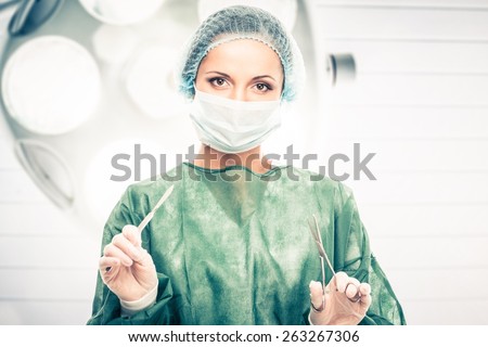 Young woman doctor with scalpel and scissors in surgery room