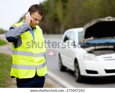 Man calling car towing service on a highway roadside