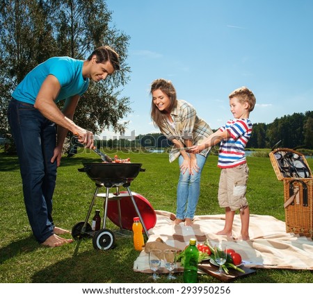 Young family preparing sausages on a grill outdoors