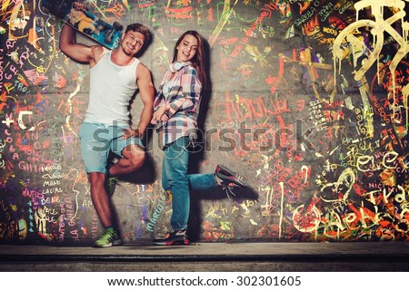 Young couple with skateboard  outdoors over graffiti painted wall