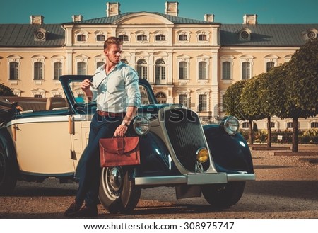 Confident wealthy young man with briefcase near classic convertible