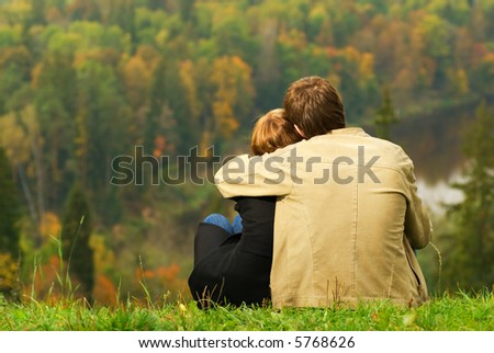 Sweet couple sitting on a hill and looking at the autumn landscape