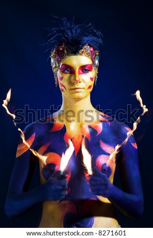 Mysterious woman with artistic body-art paint on her holding fire flames.