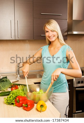 Beautiful young woman mixing vegetable salad in a glass bowl