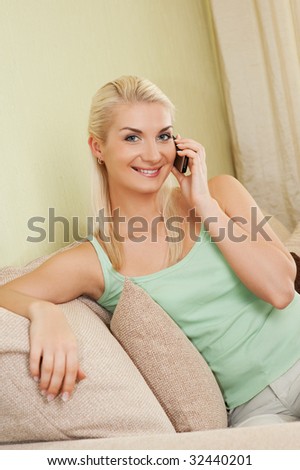 Happy young woman sitting on sofa and talking on phone