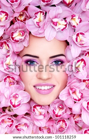 Portrait of young beautiful smiling woman with stylish make-up and pink orchids around her face