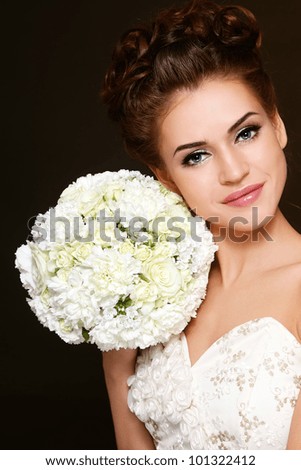 Portrait of young beautiful happy bride with stylish make-up and hairdo holding bouquet in her hand