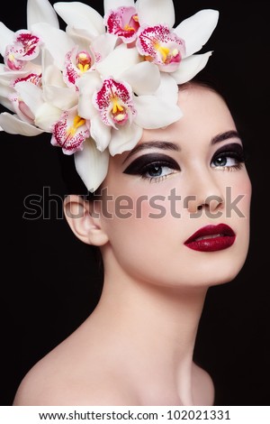 Portrait of young beautiful woman with stylish fancy make-up and orchids in her hair