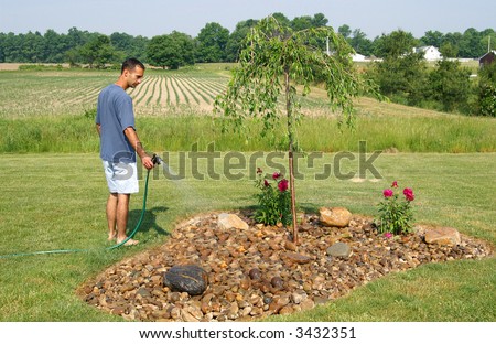 A man watering his flower bed on a sunny hot day