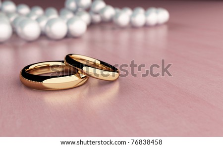 Two golden rings on wood table with pearl beads