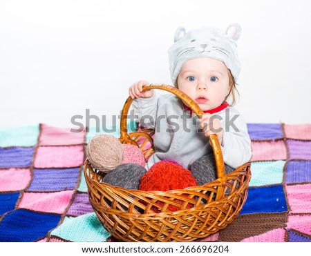 Little boy dressed as a cat sitting in basket with balls of wool