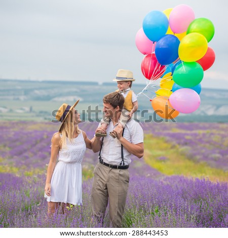 Happy young family of three person walking on lavender field with color balloons