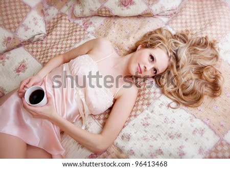 Beauriful girl in nightgown drinking coffee on bed