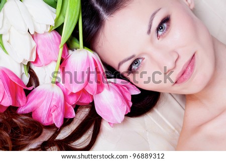 Beautiful brunette girl laying in bed with tulip flowers