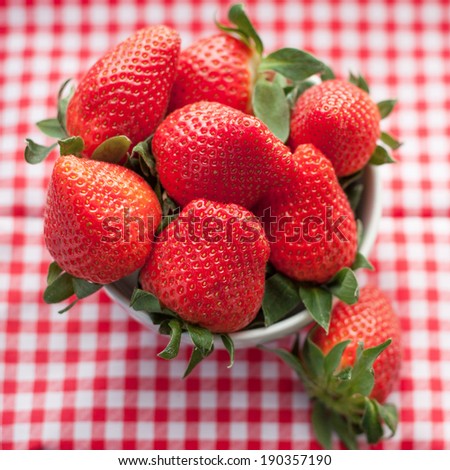 Small bowl filled with succulent juicy fresh ripe red strawberries on table with red checkered tablecloth