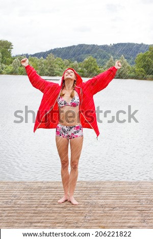 Girl in a red rain jacket and bikini enjoy the rain