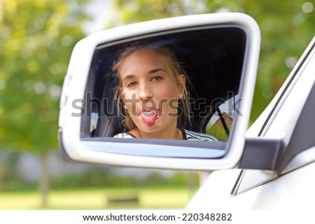 Young woman sticking tongue out in side mirror