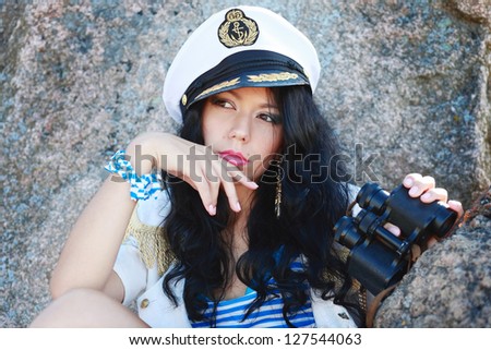 Portrait of beautiful female dressed as a sailor is looking left and holding her hand near the face