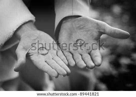 Two hands are holding wedding rings. Man is holding brides engagement ring and woman is holding grooms ring
