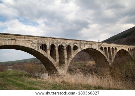 Old stone middle age bridge in Bulgaria, against a cloudy sky
