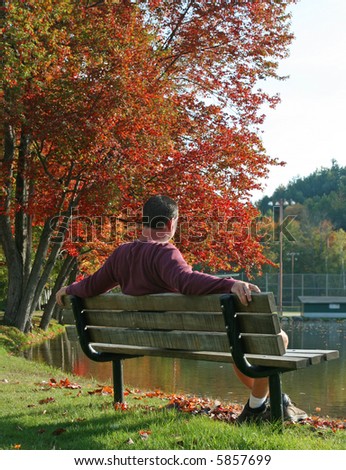 Casual man relaxing on park bench along pond with autumn trees
