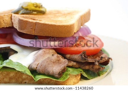 Hot roast beef sandwich with melted cheese, lettuce, tomato, and red onion on a plate with white background