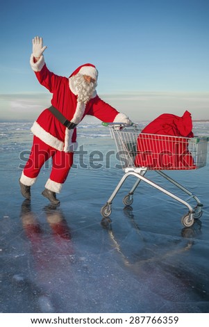Santa Claus carries a shopping cart with gifts in a sack on a winter lake ice
