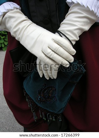 Close up of a woman\'s hands in white leather gloves, holding a vintage handbag. Notice the ruffled cuffs and pantaloons.