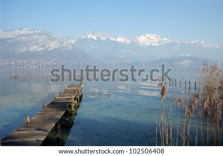 Wood pontoon, water, reeds bed and snowed mountains on Annecy lake, France