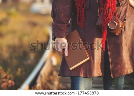 Young girl in leather coat with book walking along railroad in sunshine, sunrise