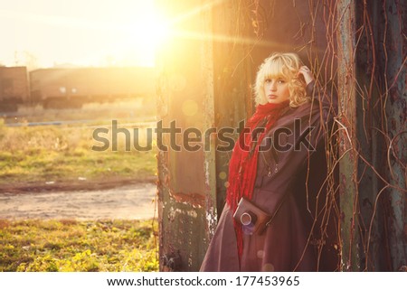 Young girl in leather coat with camera near railroad in sunshine, sunrise