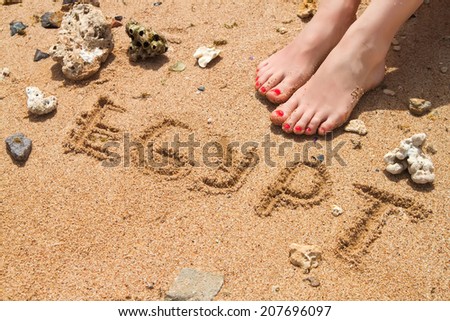 female feet with red pedicure in beach sand with text egypt