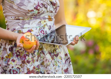 young woman eat apple and play on tablet pc in park