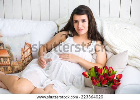 pretty pregnant woman drinking water while lying on a sofa at home