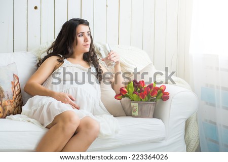 pretty pregnant woman drinking water while lying on a sofa at home