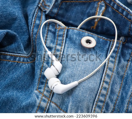 Pair of white ear-in headphones forming a heart shape in a blue pocket denim jacket