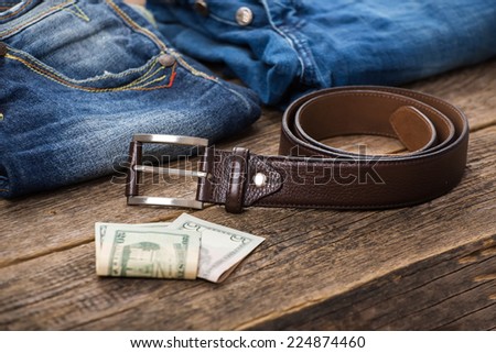 Dirty jeans, money and belt on wooden floor