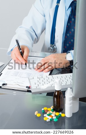 Doctor on his workplace with computer, pills, tablets, write a prescription patient data history